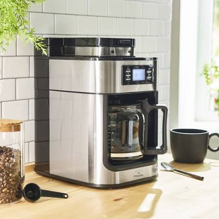 Cafetière argentée et noire avec écran en façade et carafe en verre sur un plan de travail